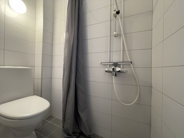Un baño con inodoro, ducha con cortina y grifo empotrado en la pared.