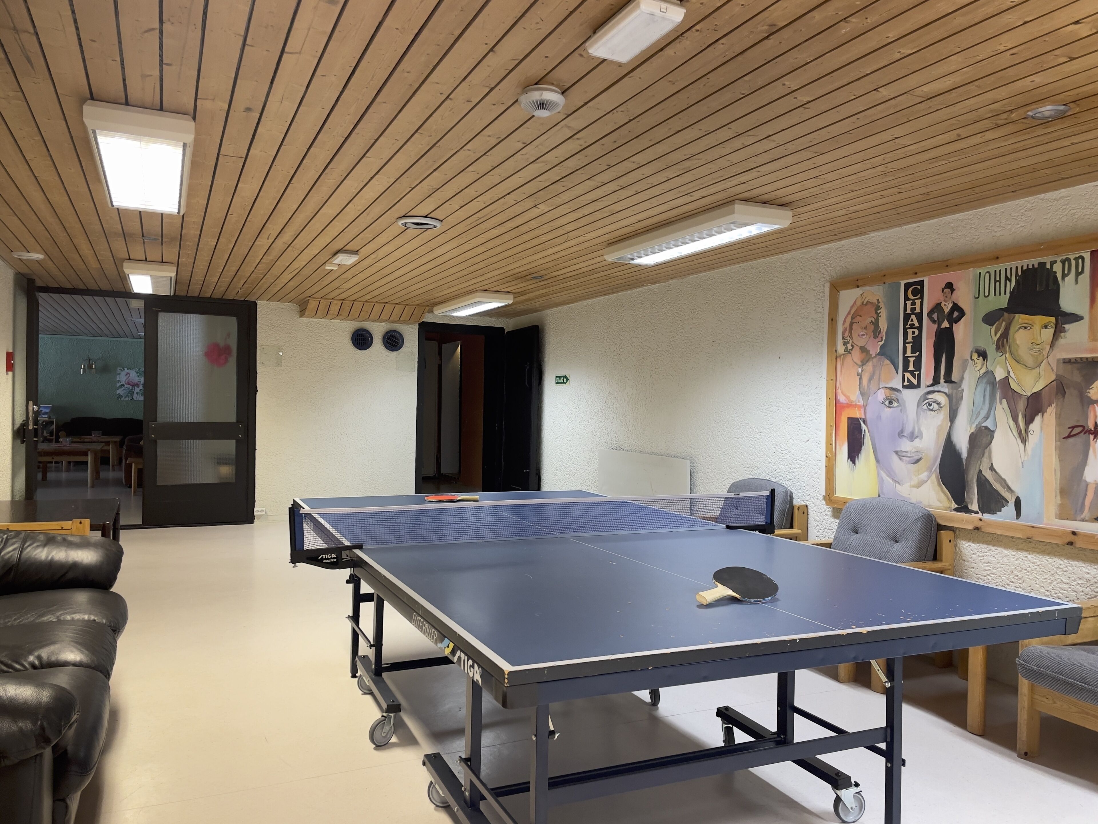 A ping pong table in a room with a wooden ceiling and a painting on the wall.