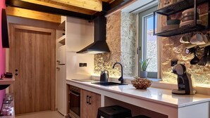 A modern kitchen with a stone backsplash, wooden cabinets, a black range hood, and a coffee machine. - Vin Dimora Suites with shared pool - Vino Roze (Ano Archanes)