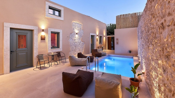 A poolside area with a pool, seating, and a stone wall. - Vin Dimora Suites with shared pool - Vino Roze (Ano Archanes)