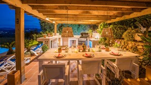 An outdoor dining area with a wooden pergola, a pool, and a stone wall. - 3 Bedroom Family Villa with Pool (Javea / Xàbia)