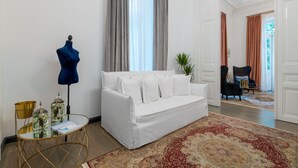 A white sofa in a room with a patterned rug, a blue lamp, and a mannequin. - Superior Suite Theseus by 2 Mazi Suites (Athina)