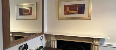A room with a fireplace, a mirror, and two framed artworks on the wall.