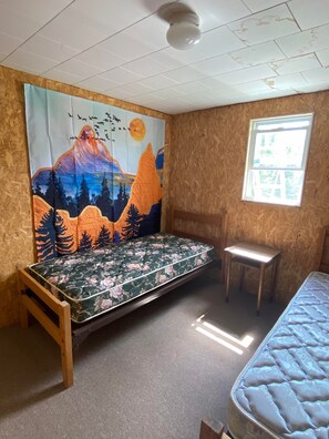 A room with a bed, a small stool, a window, and a tapestry. - The Lodge-Aroostook County, Maine. (Castle Hill)