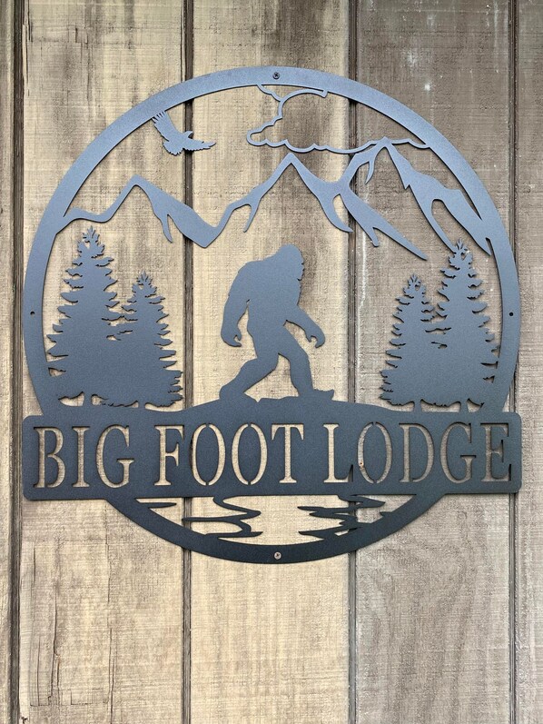 A metal sign with a silhouette of a hiker and trees, labeled "BIG FOOT LODGE". - The Lodge-Aroostook County, Maine. (Castle Hill)