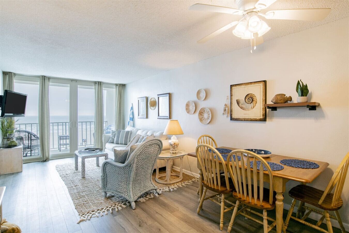 A spacious living area with a balcony, a dining table with chairs, and a television on a stand.