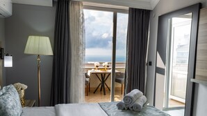 A hotel room with a bed, a lamp, a table with chairs, and a view of the sea through a glass door. - LİFE POOL SUİTE HOTEL (Trabzon)