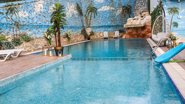 A swimming pool with a tiled edge, a slide, lounge chairs, and decorative plants. - LİFE POOL SUİTE HOTEL (Trabzon)