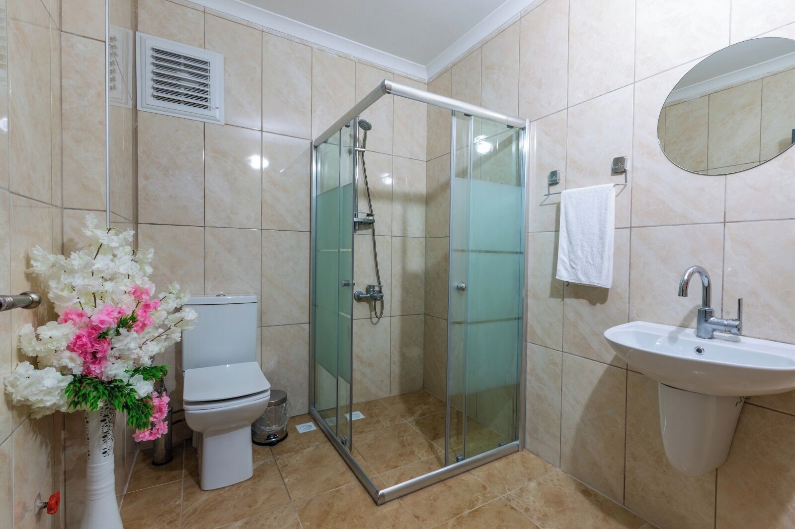 Un bany amb dutxa envidriada, un vàter, un lavabo i un ram de flors.