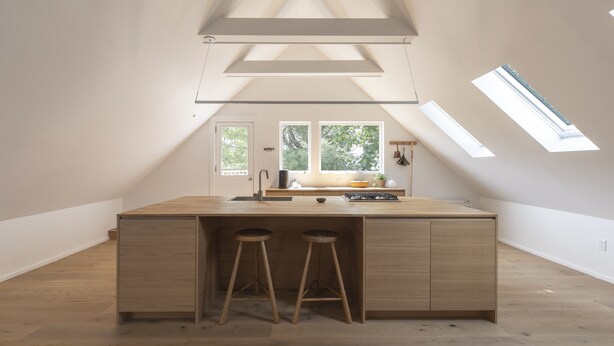 A modern kitchen with a central island, two stools, skylights, and a view of the outdoors.