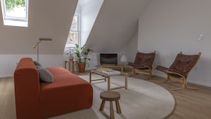 A modern loft-style living room with a red sofa, wooden chairs, a small round table, and a TV.