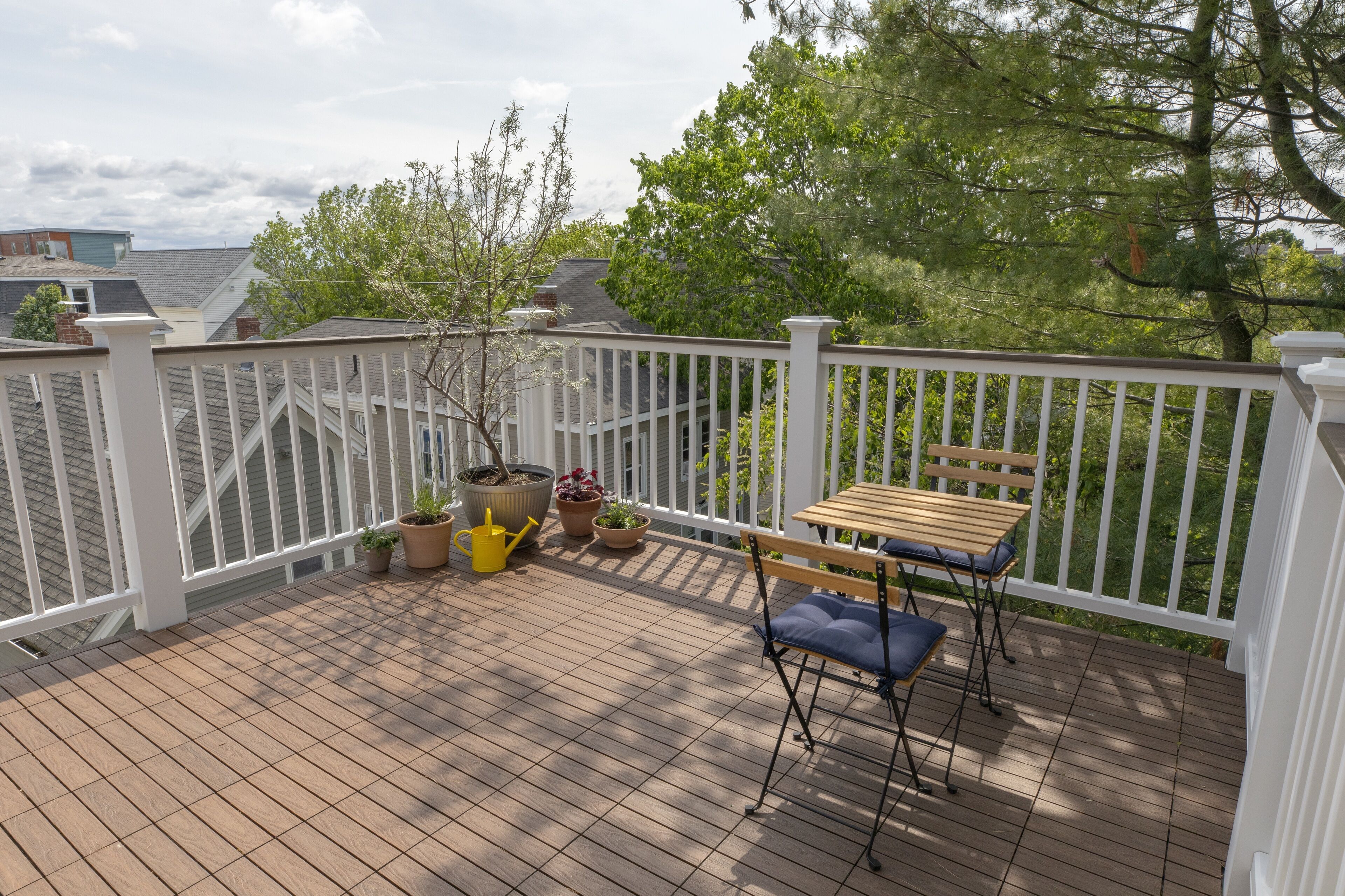 Een houten terras met een witte balustrade, een tafel met een bankje en plantenpotten.
