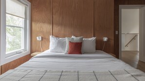 A bedroom with a wooden headboard, a large window, and a bed with white bedding and decorative pillows.