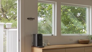 A modern kitchen with a wooden countertop, two windows with a view of trees, and a coffee maker on the counter.