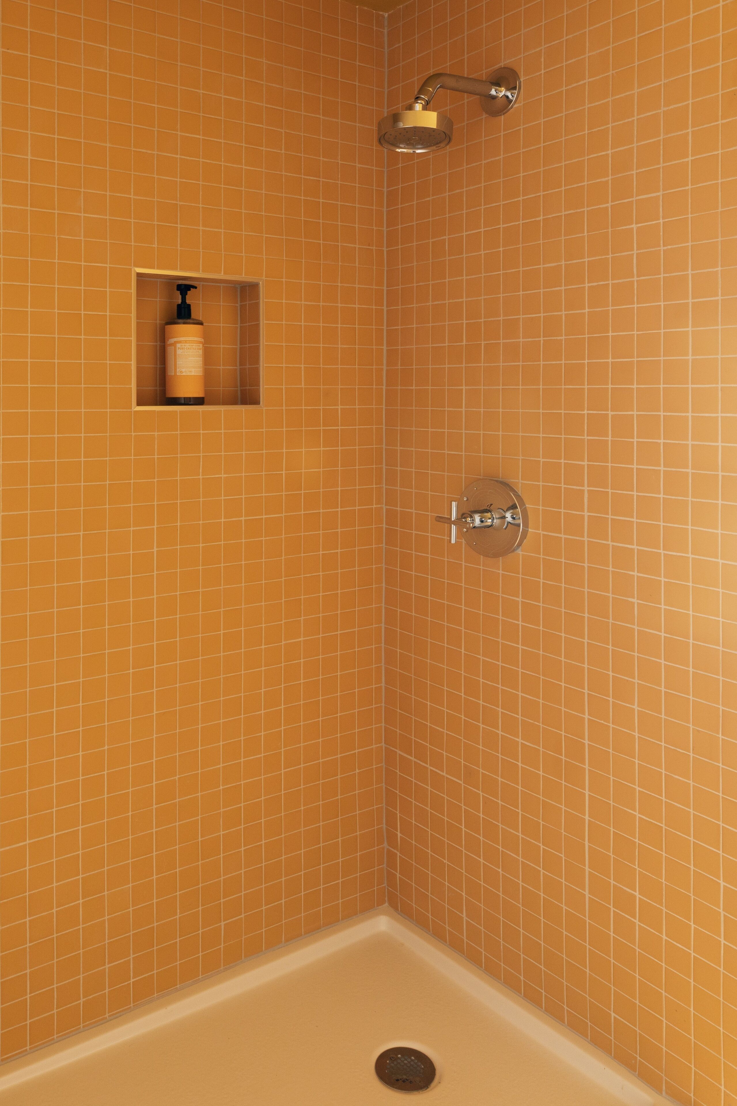 A corner shower with orange tiles, a soap dispenser, and a showerhead.