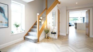 Ein geräumiger Flur mit einer Holztreppe, einem großen Spiegel und einer modernen Leuchte.