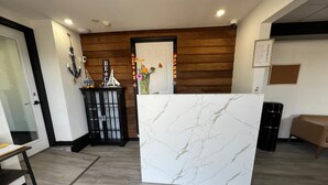 A reception area with a marble counter, wooden paneling, a black cabinet with decorative items, and a bench. - Harborside Suites (South Yarmouth)
