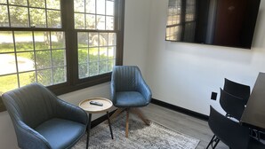 A modern room with two blue armchairs, a small round table with a remote, a patterned rug, and a TV on the wall. - Harborside Suites (South Yarmouth)