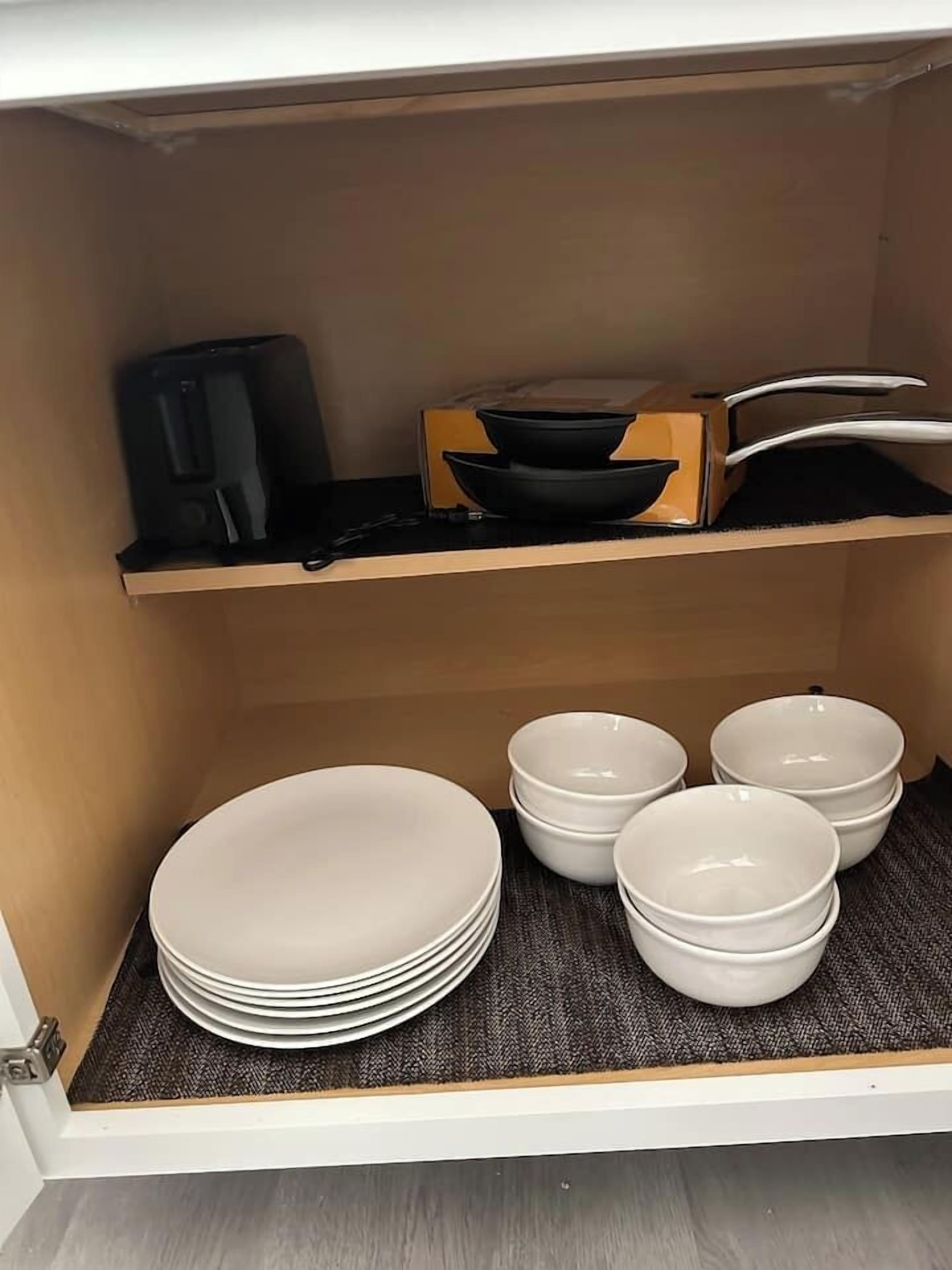 A kitchen cabinet with a black appliance, a wooden box, and stacked white plates.