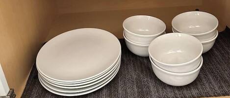 A kitchen cabinet with a black appliance, a wooden box, and stacked white plates.