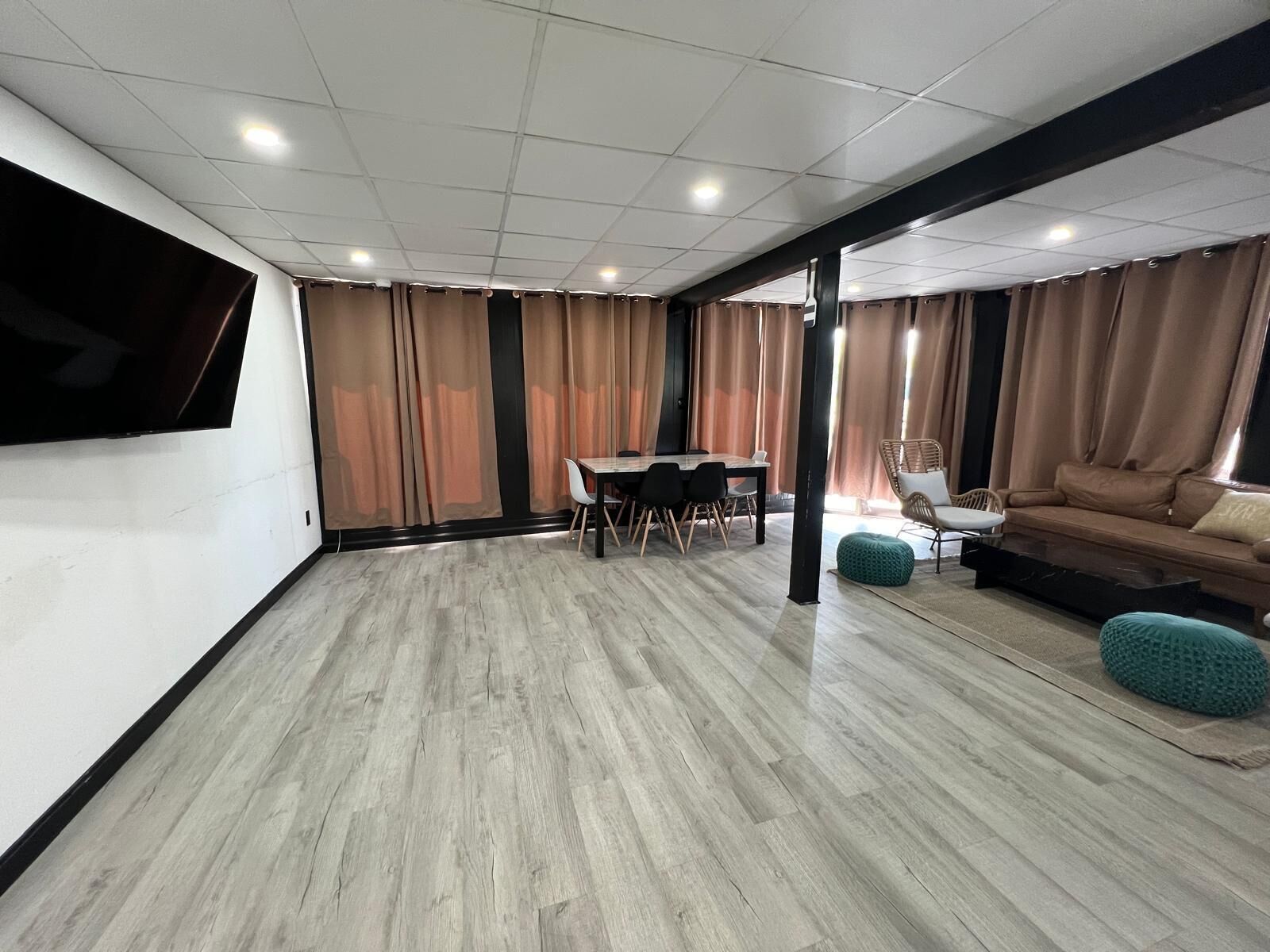 A spacious room with a dining area, a sofa, and a TV mounted on the wall.