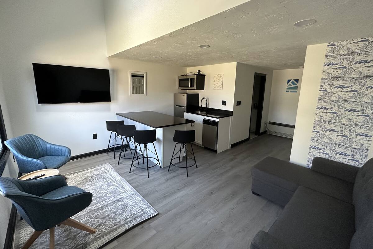 A modern living room with a grey sofa, a blue armchair, and a dining area with a kitchen in the background.