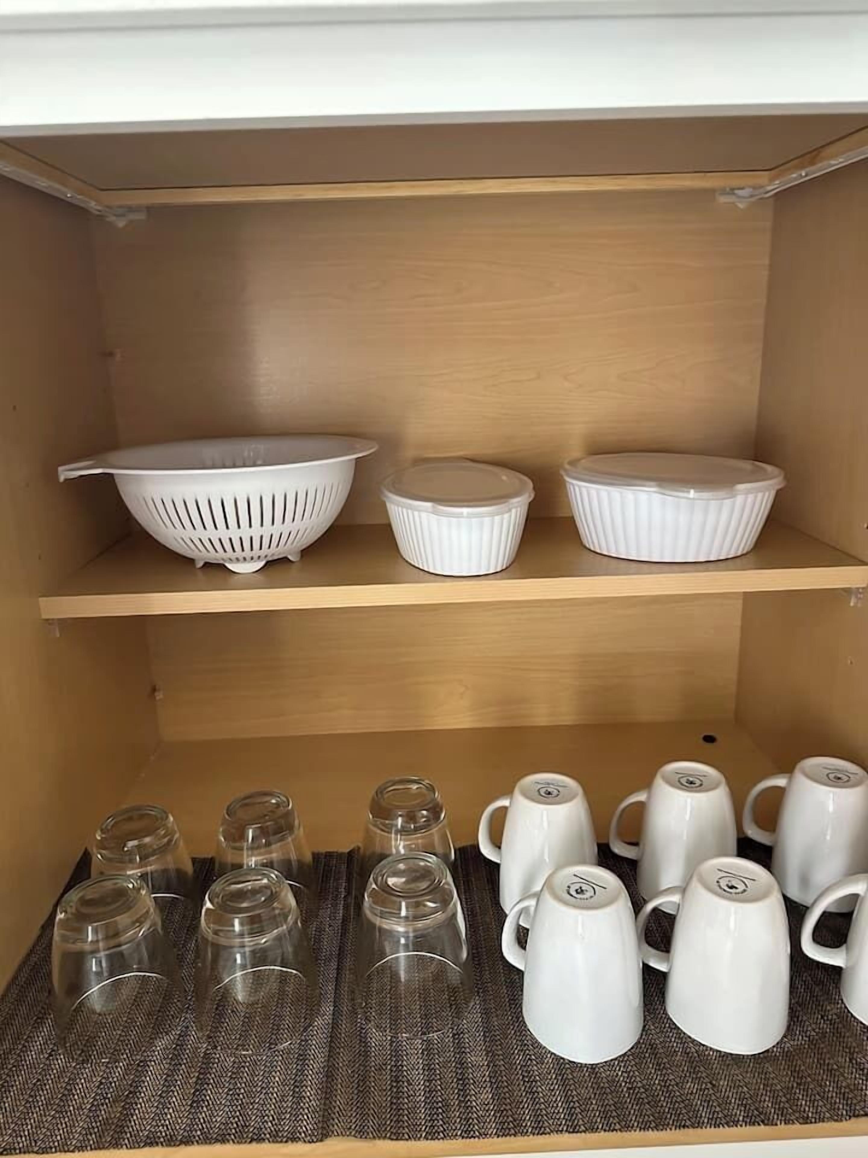 Une étagère de cuisine avec des passoires blanches, des bols et un tapis tressé sur lequel sont posés des verres et des tasses.