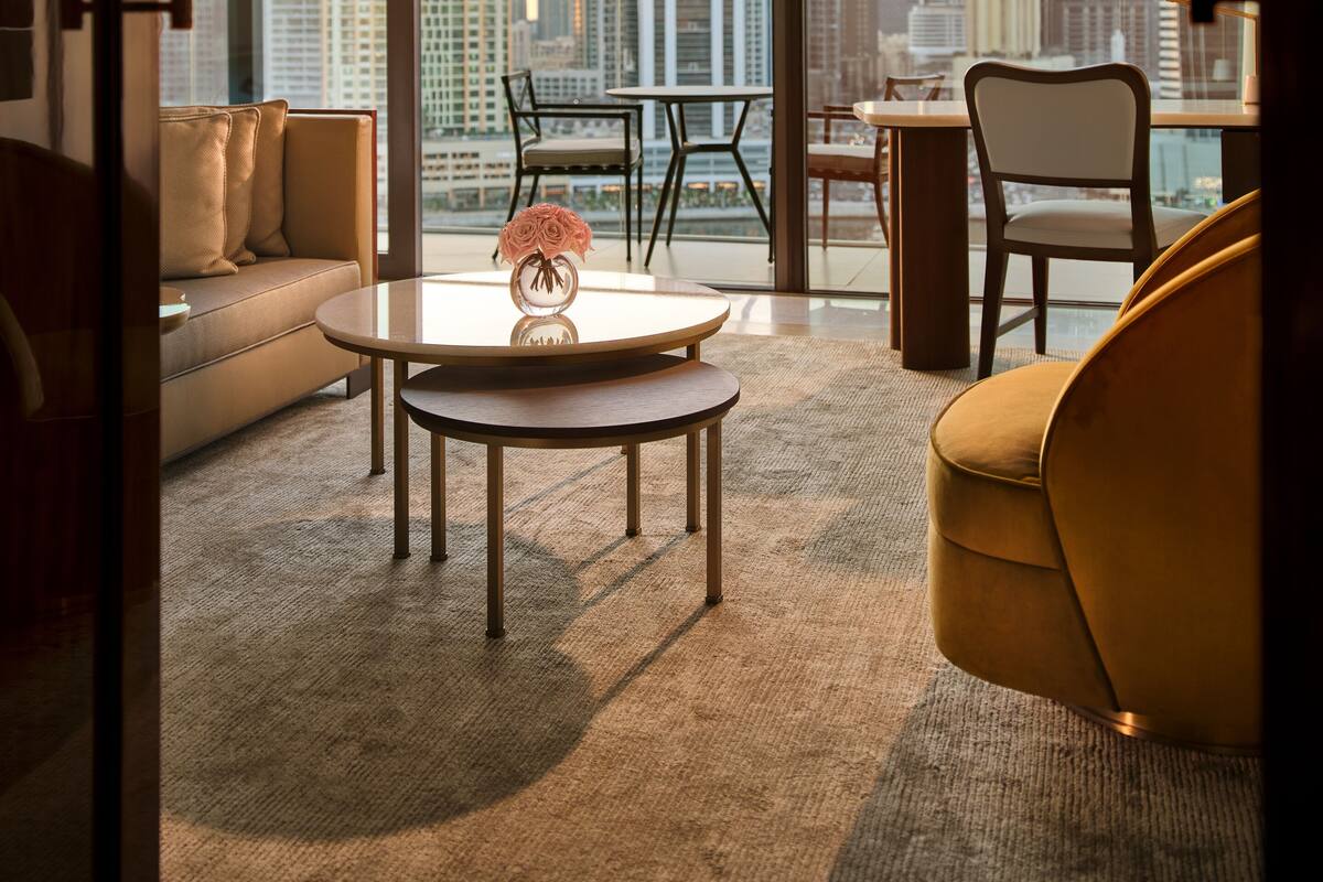 A modern living room with a sofa, a coffee table, and a chair, featuring a city view through large windows.