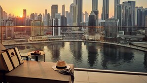 A city skyline at sunset with a view of the water and a lounge area with a hat and a bag. - The Lana - Dorchester Collection (Dubai)