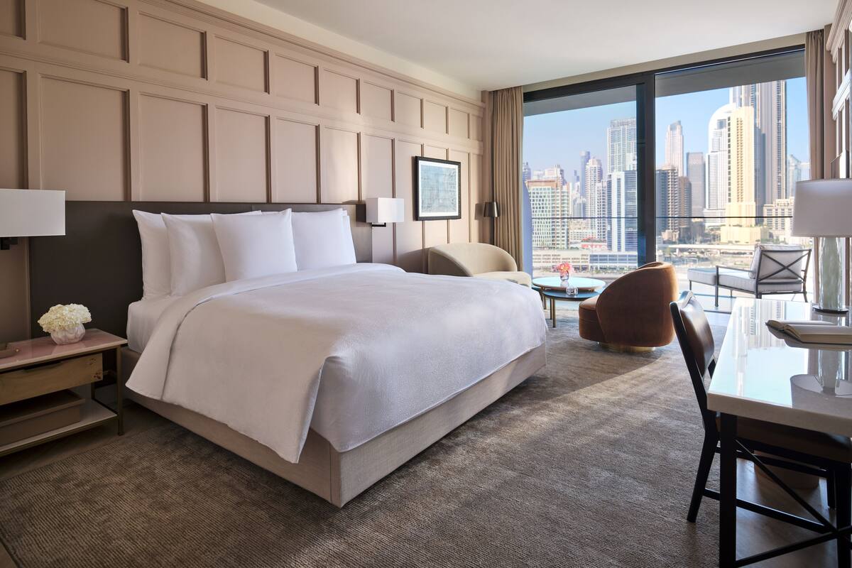 A hotel room with a large bed, a desk, and a view of the city skyline.