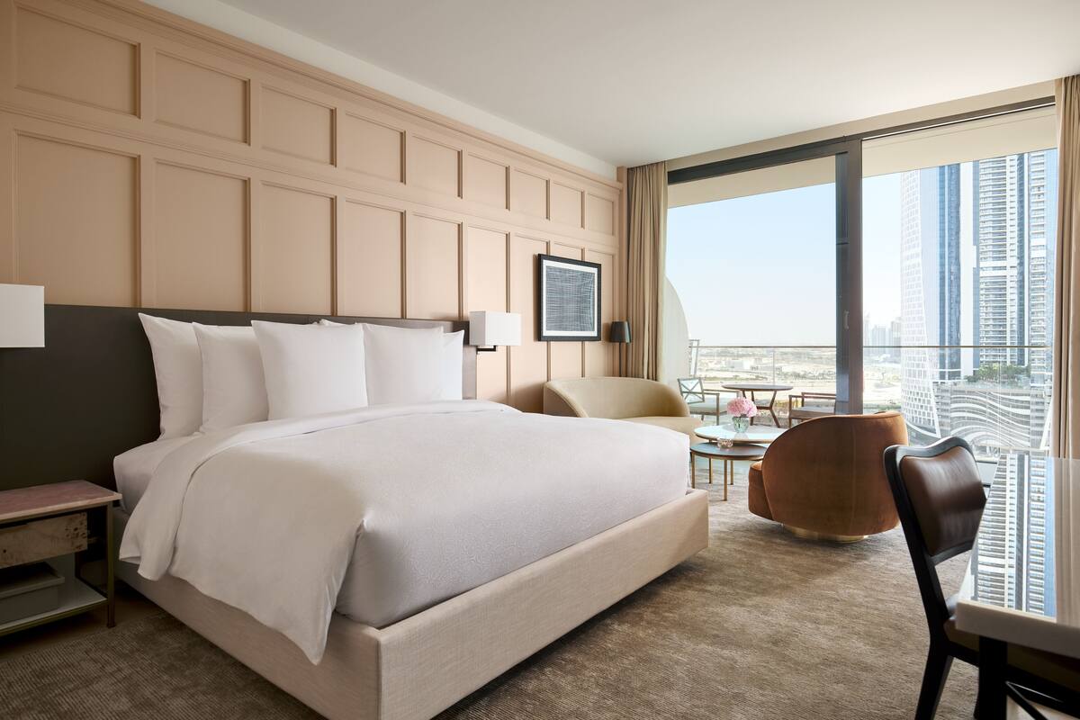 A modern hotel room with a large bed, a desk, and a view of a cityscape.