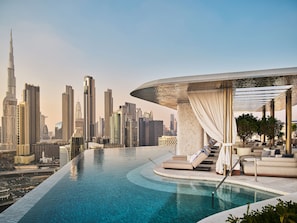 A rooftop infinity pool with a city skyline view, a covered seating area, and a modern architectural design.