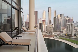 A balcony with lounge chairs overlooking a cityscape and a body of water.