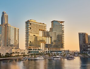 A modern high-rise hotel with multiple balconies, a marina with yachts, and a clear view of the surrounding cityscape.