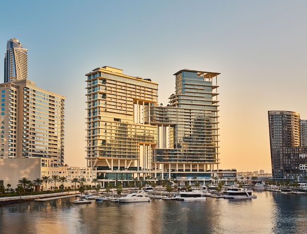 A modern high-rise hotel with multiple balconies, a marina with yachts, and a clear view of the surrounding cityscape.