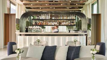 A bar area with a bartender, seating with vases of flowers, and a modern ceiling design.