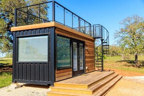 A modern cabin with a balcony, a staircase, and a wooden deck.