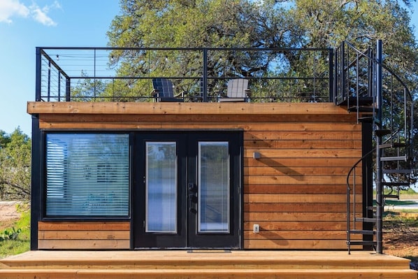 A modern cabin with a wooden exterior, large sliding glass doors, and a metal balcony.