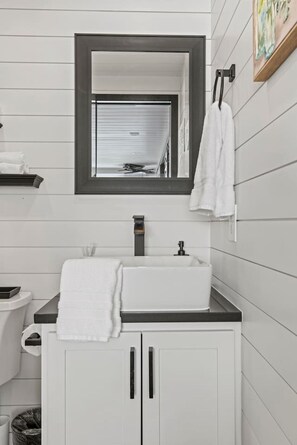 Ein Badezimmer mit einem weißen Waschbecken, einem Spiegel, einem Handtuchhalter und einer Toilette.