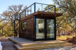 Eine moderne Holzhütte mit Glastür, einer Holzdielen-Terrasse und einer Metalltreppe.