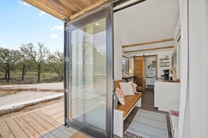 A modern cabin with a sliding glass door leading to a wooden deck and a cozy interior with a kitchen and seating area.