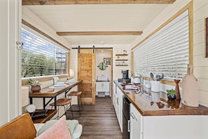 A compact kitchen with wooden beams, a dining area with stools, and a view through a window.