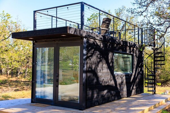 Uma cabana moderna com porta de vidro, uma pequena janela e escada de metal.