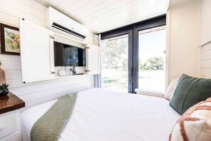 A bedroom with a bed, a TV mounted on a wall, a window, and a door.