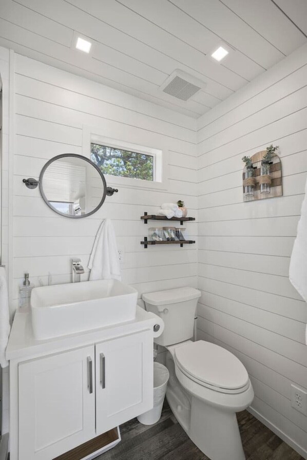 A bathroom with a white vanity, a toilet, a mirror, and wooden shelves.