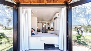 Quarto aconchegante com cama, escrivaninha e pequena cozinha.