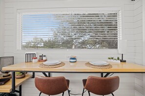 A dining area with a wooden table, two chairs, a window with blinds, and a view of trees. - New! Oak Grove-Container Retreat (Fredericksburg)