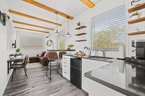 Et moderne køkken med en central ø, træbjælker, hængende lamper og indbyggede hylder.