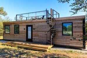 Eine moderne Holzlaube mit einer Metalltreppe, einer Tür und zwei Fenstern.