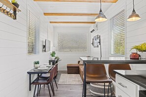 A modern kitchen with white cabinetry, a dining area with a wooden table and chairs, and pendant lighting. - The Texas Longhorn-Luxe CargoHome | Rooftop patio (Fredericksburg)